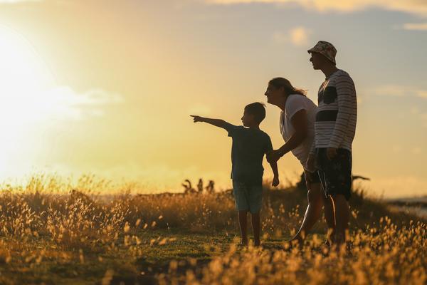 Two adults and a child stand in a field watching the sunset