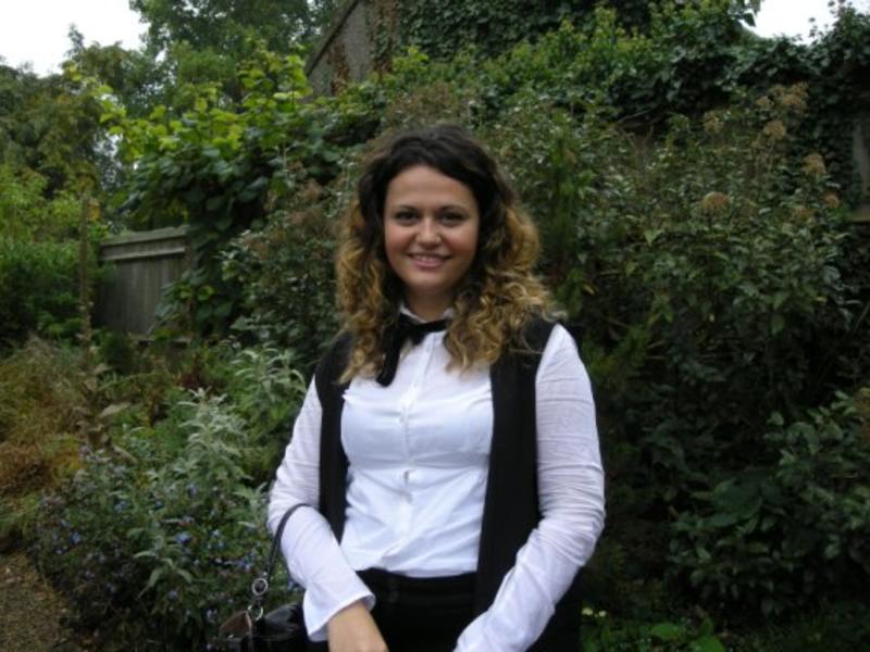 Aslı Mert stands in a garden, wearing Sub Fusc before her Matriculation ceremony. 